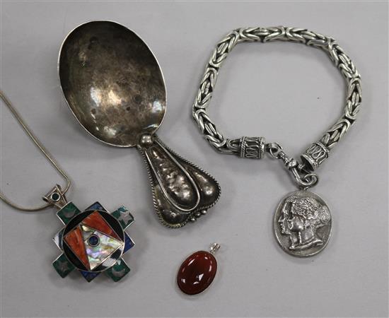 An Arts & Crafts white metal caddy spoon, a silver commemorative bracelet, a silver and enamel pendant & one other pendant.